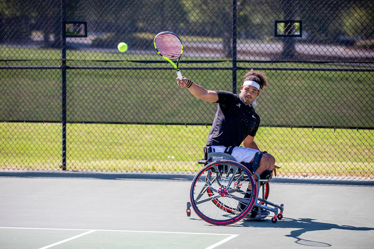 A wheelchair tennis player hits a backhand shot.