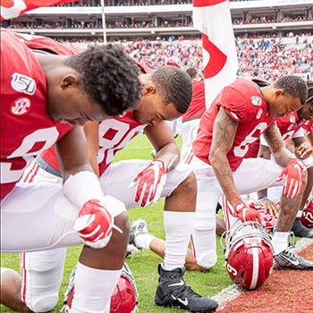 Football players kneel in prayer at the goal line at Bryant-Denny stadium